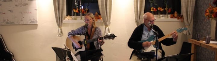 Om oss – STEP UP på scen Närbild på STEP UP-duon under spelning – sång, akustisk gitarr och elgitarr.